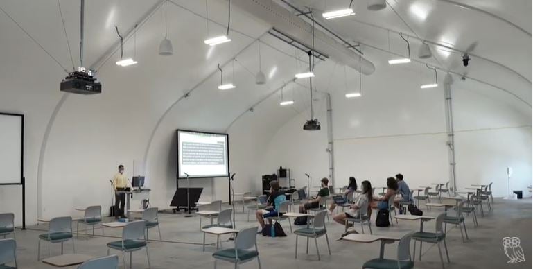 University classroom in large, hangar-like tent. Teacher and six students.